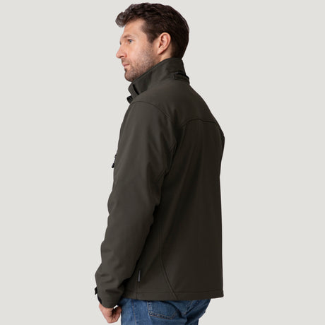 [Vince is 6'1" wearing a size Medium.] Man wearing Free Country Men's Odyssey II Flex Super Softshell® Jacket in dark green with a full front zipper opening, adjustable cuff openings, and wind and water resistant stretch performance fabric, light grey background. Perfect men’s jacket for fall weather.