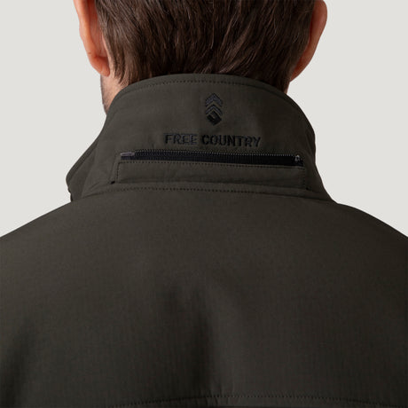 [Vince is 6'1" wearing a size Medium.] Man wearing Free Country Men's Odyssey II Flex Super Softshell® Jacket in dark green with a full front zipper opening, adjustable cuff openings, and wind and water resistant stretch performance fabric, light grey background. Perfect men’s jacket for fall weather.