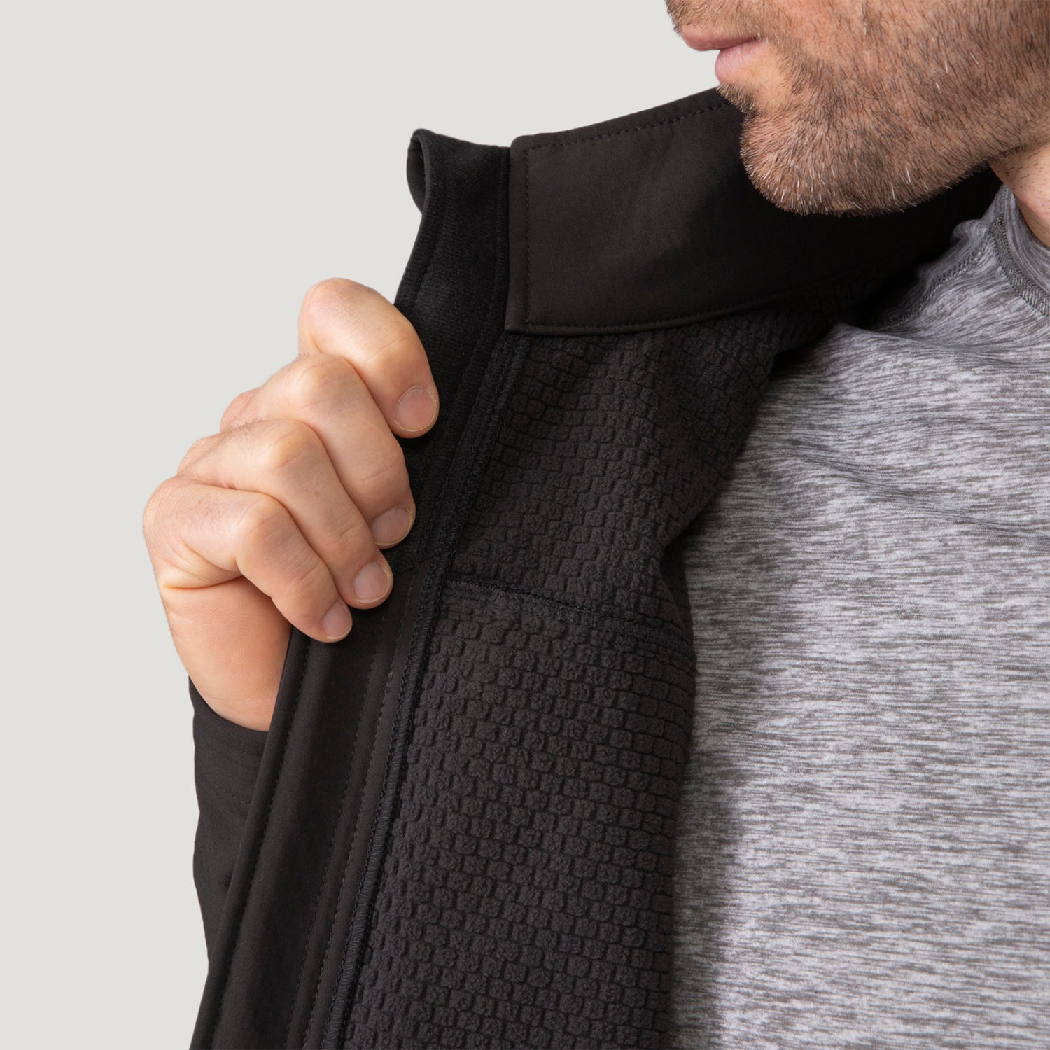 A man holds open the front of a black Men’s Stretch Super Softshell® Jacket to reveal the textured grid pattern of the interior lining.