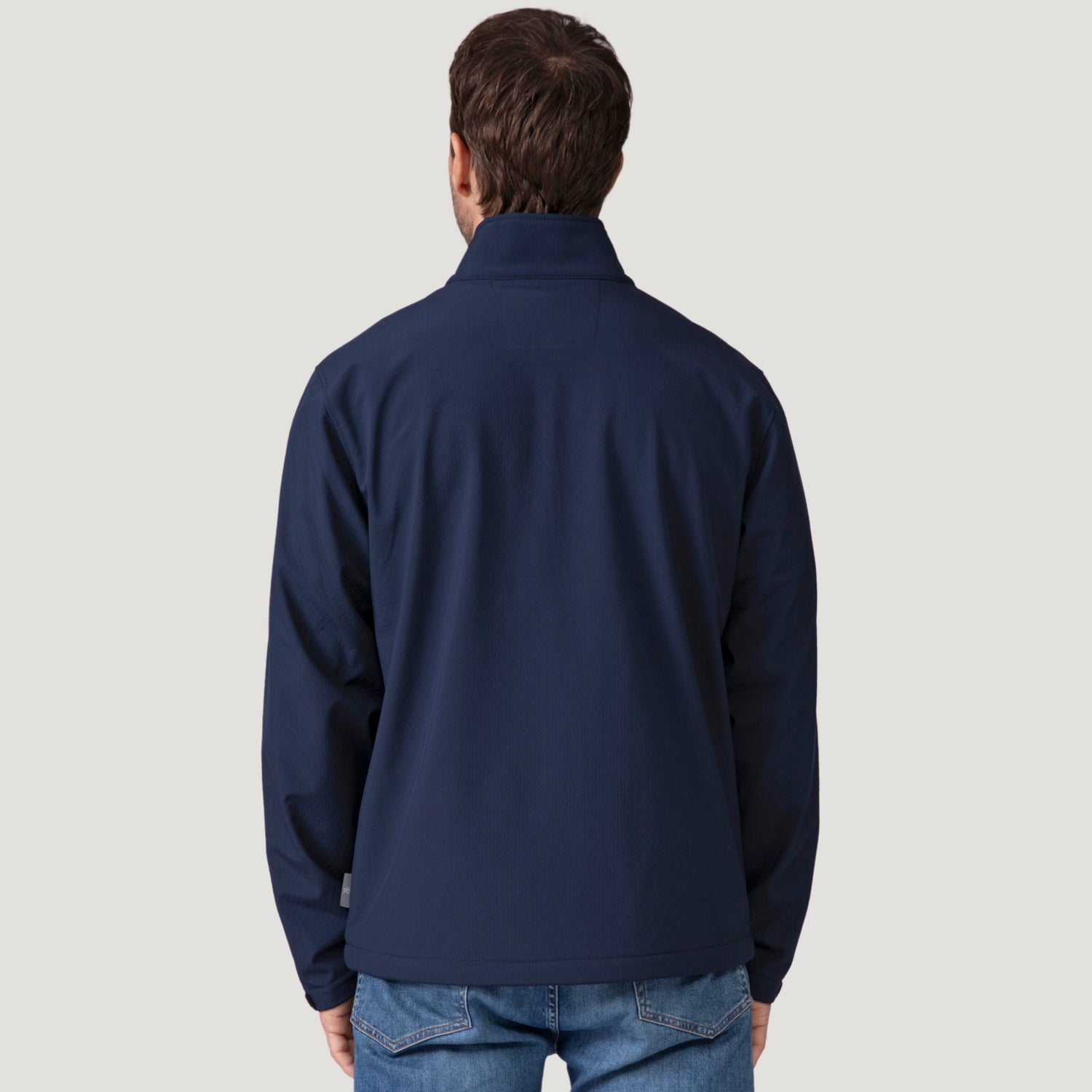 Back view of a person wearing a navy blue Men’s Stretch Super Softshell® Jacket and blue jeans.