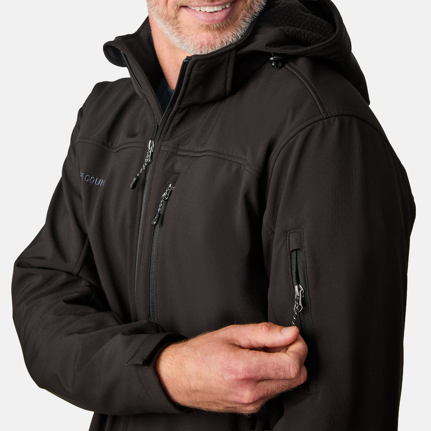 [Kolby is 6'2" wearing size M.] Man wearing Free Country Men's Odyssey II Flex Super Softshell® Jacket in black with a full front zipper opening, adjustable cuff openings, and wind and water resistant stretch performance fabric, light grey background. Perfect men’s jacket for fall weather.