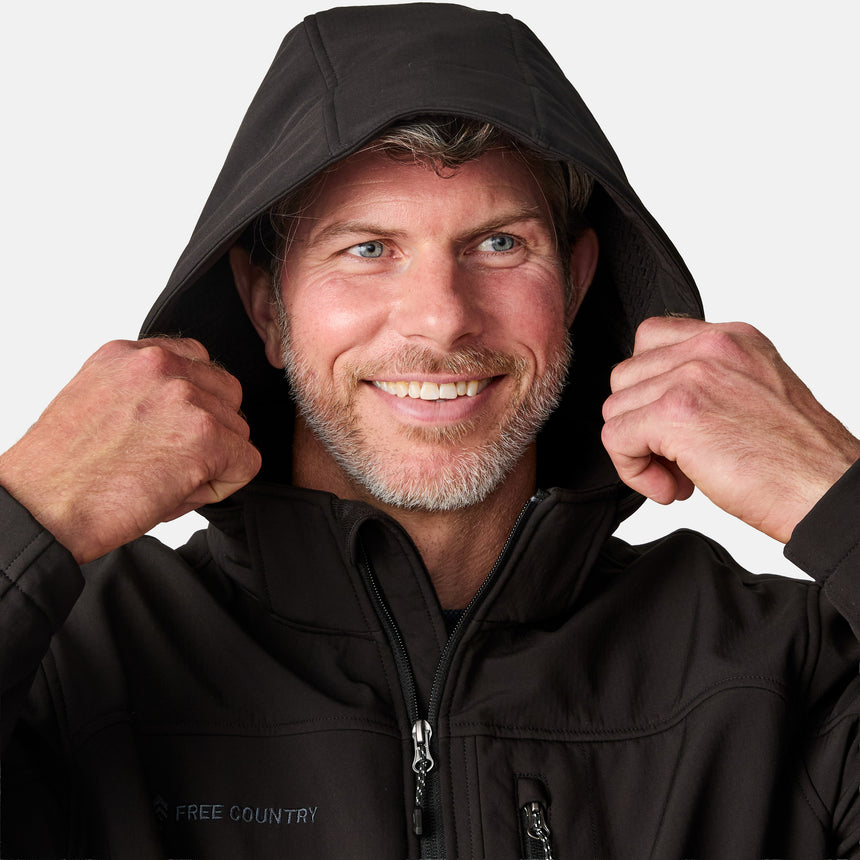 [Kolby is 6'2" wearing size M.] Man wearing Free Country Men's Odyssey II Flex Super Softshell® Jacket in black with a full front zipper opening, adjustable cuff openings, and wind and water resistant stretch performance fabric, light grey background. Perfect men’s jacket for fall weather.