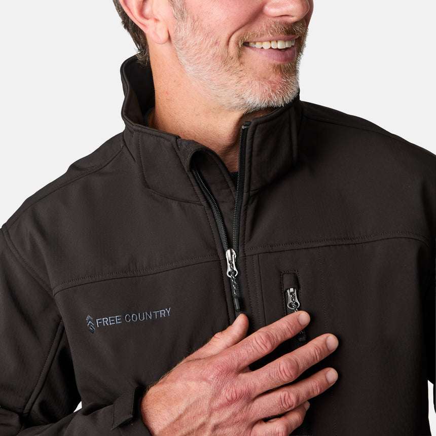 [Kolby is 6'2" wearing size M.] Man wearing Free Country Men's Odyssey II Flex Super Softshell® Jacket in black with a full front zipper opening, adjustable cuff openings, and wind and water resistant stretch performance fabric, light grey background. Perfect men’s jacket for fall weather.