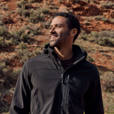 Man wearing a black hooded softshell jacket standing in a desert landscape