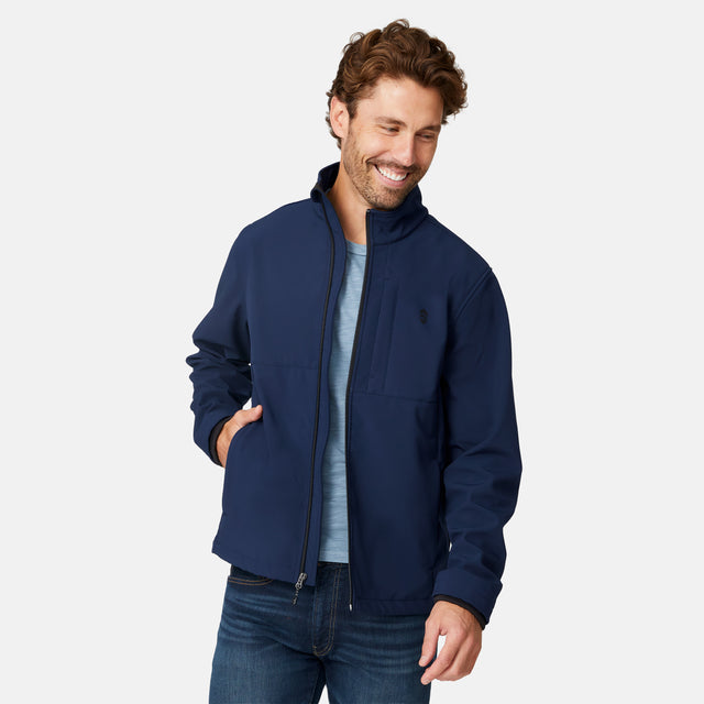 [Matt is 6'2" wearing size M.] Men’s Free Country navy zip-front softshell jacket with high stand collar and minimalistic design, worn over a light blue shirt and paired with blue jeans—delivering a clean, everyday look with subtle utility and transitional weather appeal.