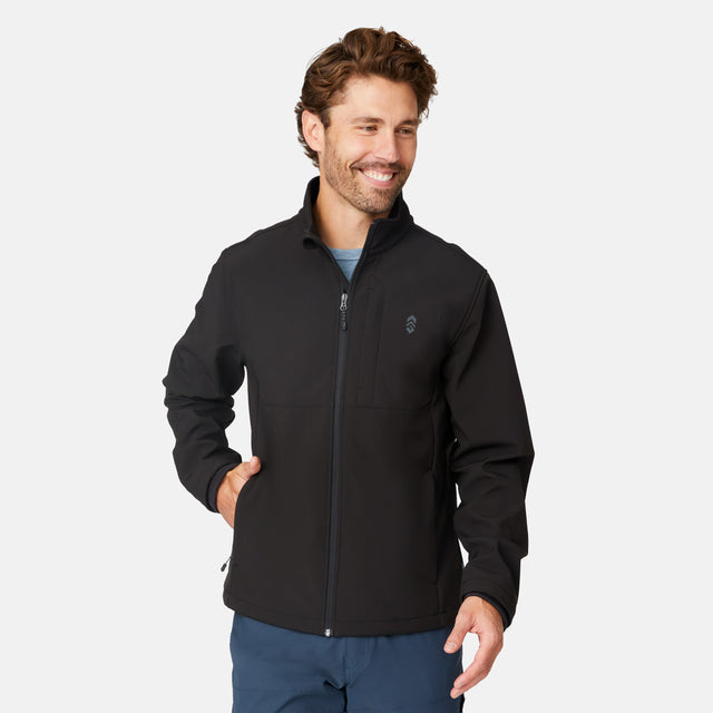 [Matt is 6'2" wearing size M.] Men’s Free Country black zip-front softshell jacket with high stand collar, subtle chest logo, and minimalistic design—featuring streamlined silhouette and long sleeves. Worn with blue pants for a clean, versatile look suited to cool-weather outings.
