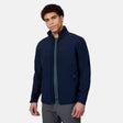 A person wears a navy Free Country Men’s Hanson II Super Softshell® Jacket, a weather-resistant, performance stretch softshell with a chest pocket and two lower side pockets.