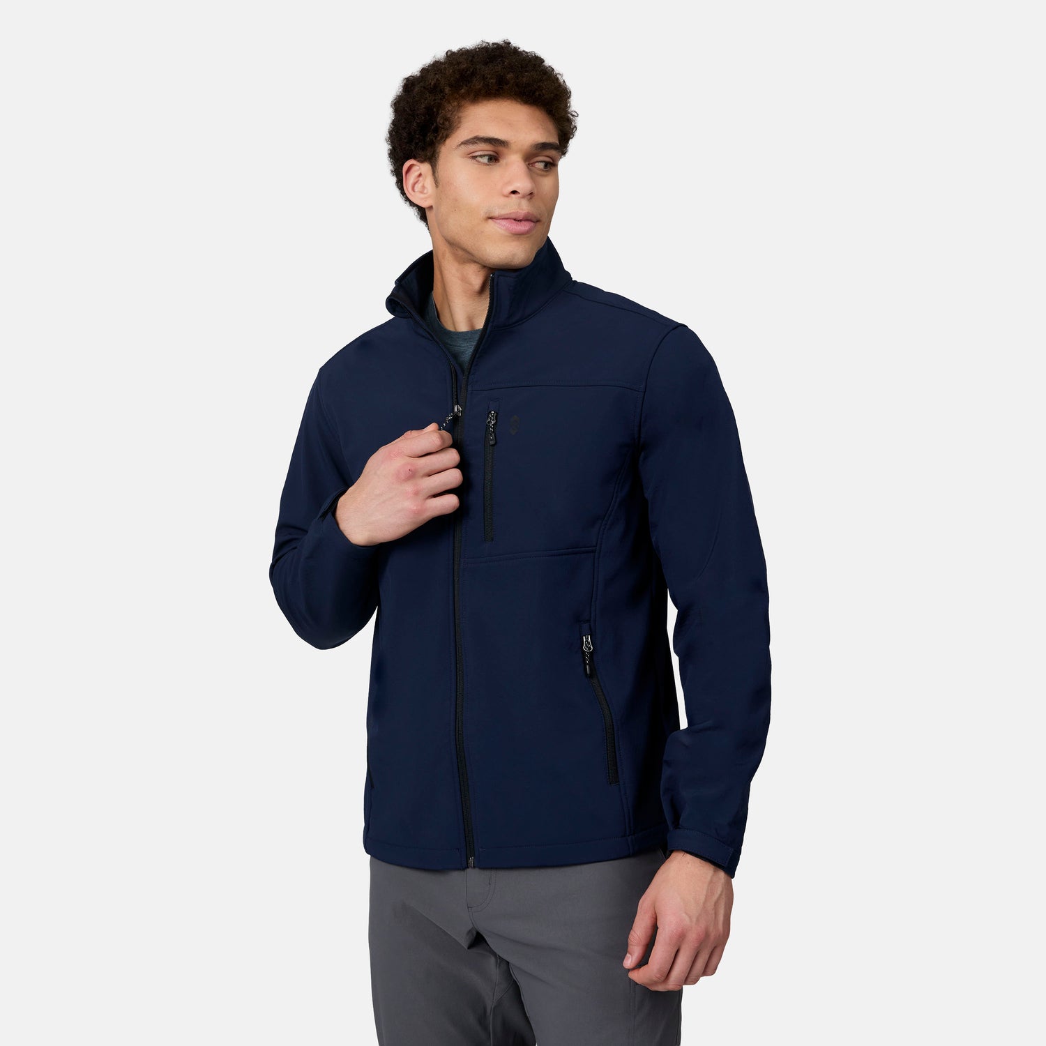 A man wearing a navy blue, weather-resistant, performance stretch Free Country Men’s Hanson II Super Softshell® Jacket with a high collar and zippered chest and side pockets.
