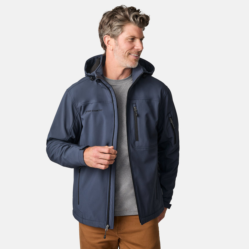 [Kolby is 6'2" wearing size M.] Man wearing Free Country Men's Odyssey II Flex Super Softshell® Jacket in blue with a full front zipper opening, adjustable cuff openings, and wind and water resistant stretch performance fabric, light grey background. Perfect men’s jacket for fall weather.