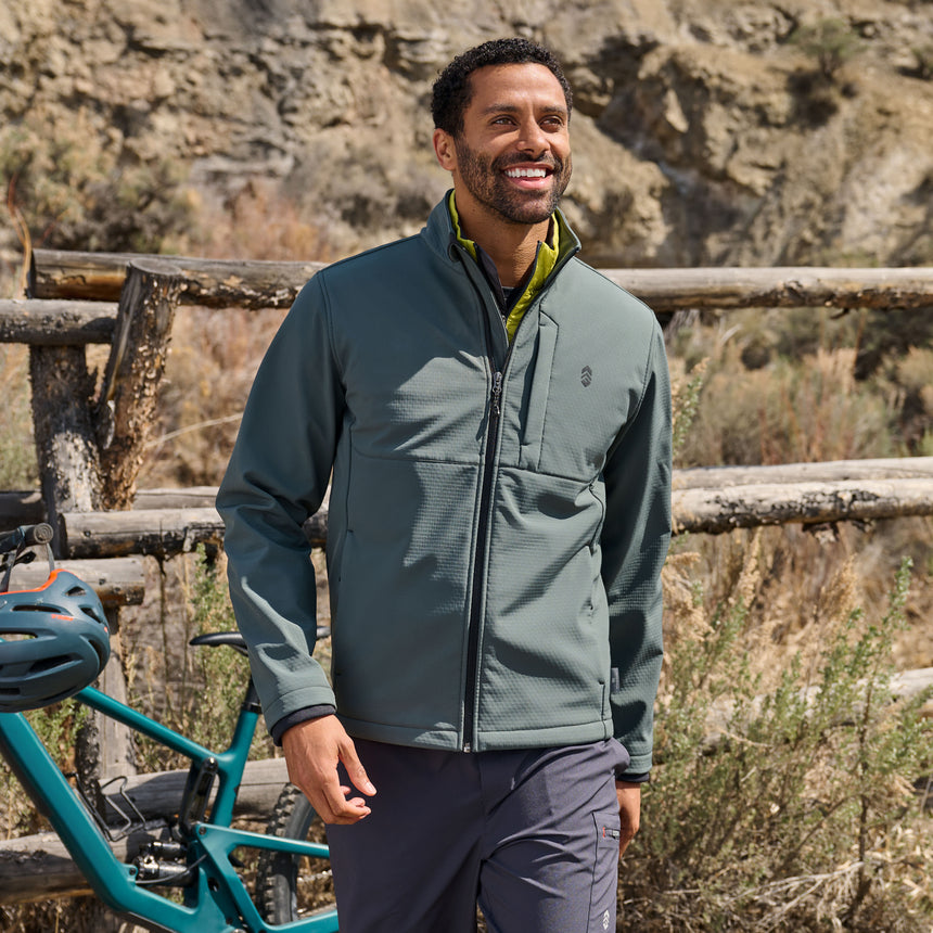 Man wearing a green jacket standing outdoors with a mountain bike in the background