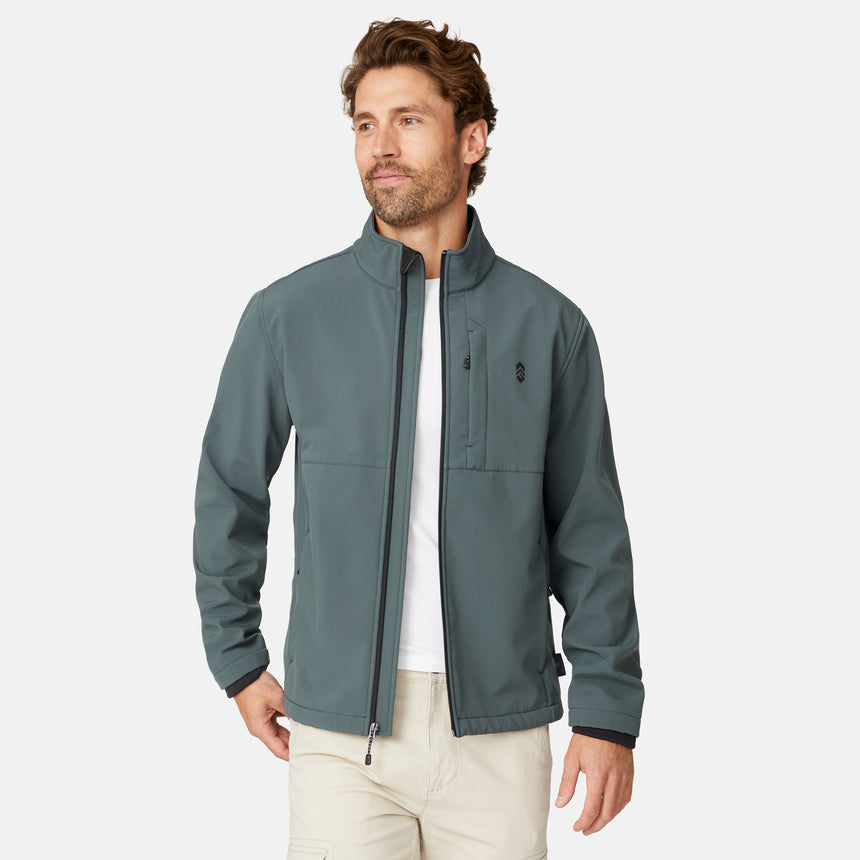 [Matt is 6'2" wearing size M.] Men’s Free Country green zip-front softshell jacket with high stand collar, subtle chest logo, and minimalistic design—featuring streamlined silhouette and long sleeves. Worn with blue pants for a clean, versatile look suited to cool-weather outings.