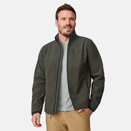 [Joe is 6'0" wearing size M.] Men’s Free Country olive green zip-front softshell jacket with high stand collar, subtle chest logo, and minimalistic design—featuring streamlined silhouette and long sleeves. Worn with blue pants for a clean, versatile look suited to cool-weather outings.