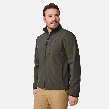 [Joe is 6'0" wearing size M.] Men’s Free Country olive green zip-front softshell jacket with high stand collar, subtle chest logo, and minimalistic design—featuring streamlined silhouette and long sleeves. Worn with blue pants for a clean, versatile look suited to cool-weather outings.