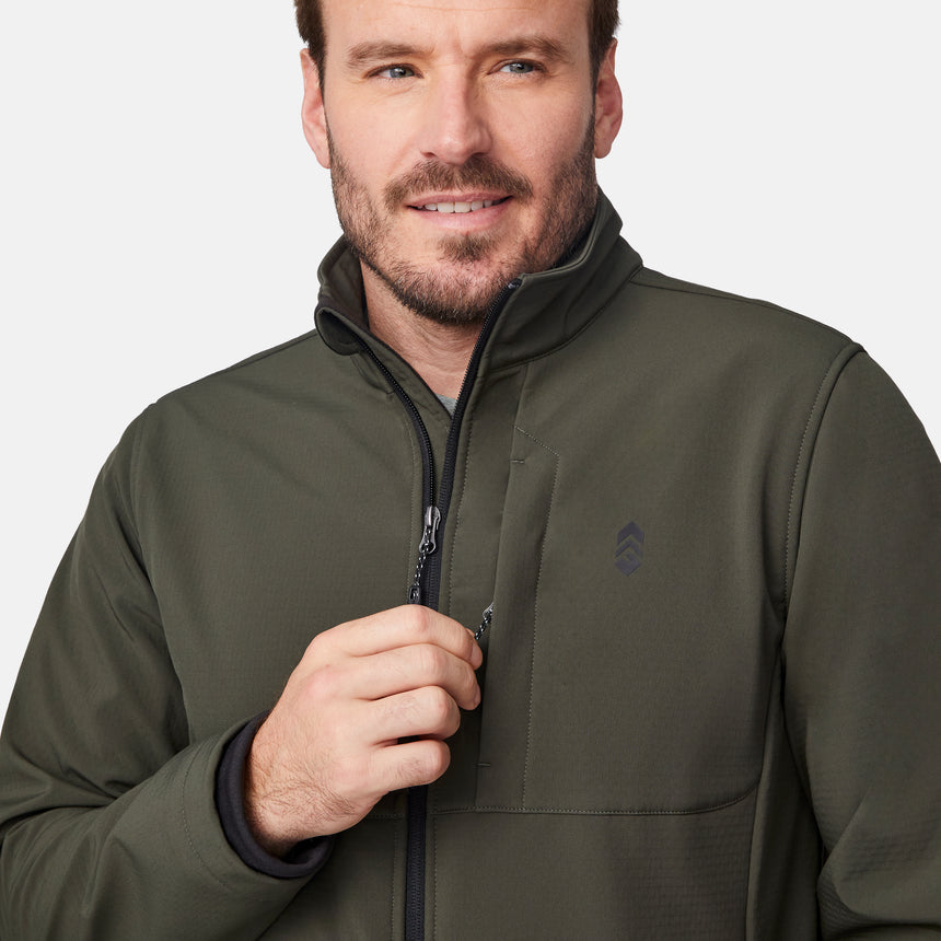 [Joe is 6'0" wearing size M.] Men’s Free Country olive green zip-front softshell jacket with high stand collar, subtle chest logo, and minimalistic design—featuring streamlined silhouette and long sleeves. Worn with blue pants for a clean, versatile look suited to cool-weather outings.