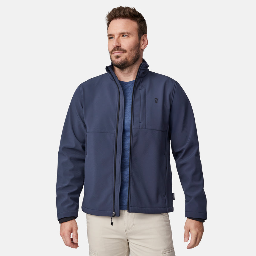 [Joe is 6'0" wearing size M.] Men’s Free Country navy blue zip-front softshell jacket with high stand collar, subtle chest logo, and minimalistic design—featuring streamlined silhouette and long sleeves. Worn with blue pants for a clean, versatile look suited to cool-weather outings.