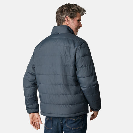 A man with short, wavy hair wears the Free Country Men's Atalaya III 3-in-1 Systems Jacket in dark gray, made from recycled REPREVE fabric, and blue jeans. He stands with his back to the camera against a plain white background.