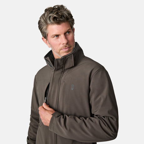 A man with wavy hair wears the Free Country Men's Atalaya III 3-in-1 Systems Jacket, made from water-resistant recycled REPREVE fabric, looking left as he unzips a chest pocket against a plain white background.