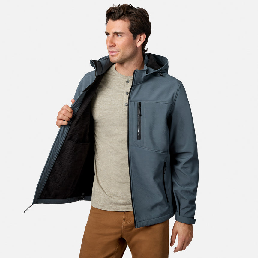 [Model is wearing size M.] A man wearing a slate blue-gray hooded jacket over a beige henley shirt and brown pants, holding the jacket open to show the black interior lining, against a light gray studio background.