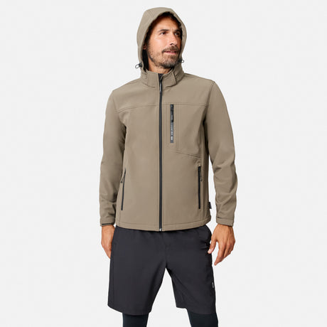 [Model is wearing size M.] A man wearing a light brown hooded softshell jacket with black zippers and dark gray athletic shorts, standing against a light gray background.