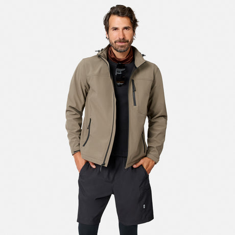 [Model is wearing size M.] A man wearing a light brown softshell jacket with black zippers, a black t-shirt, and black shorts, standing against a light gray background.