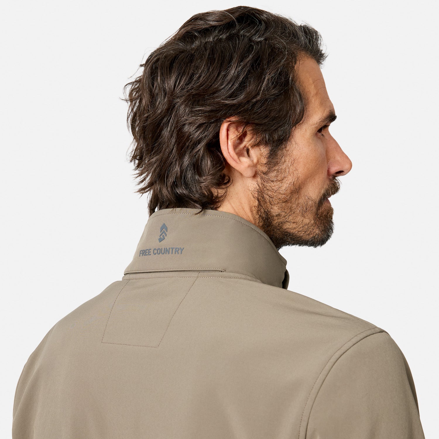 [Model is wearing size M.] A man shown from the back and side profile wearing a light beige technical pullover jacket with a high collar. The brand name 'FREE COUNTRY' is printed in blue on the inside of the collar.