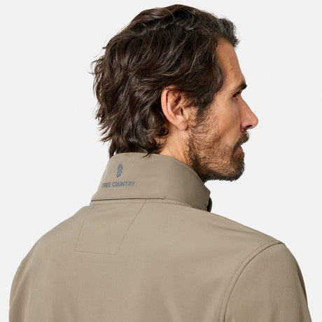 [Model is wearing size M.] A man shown from the back and side profile wearing a light beige technical pullover jacket with a high collar. The brand name 'FREE COUNTRY' is printed in blue on the inside of the collar.