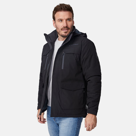 [Joe is 6'0" wearing size M.] Men’s Free Country black hooded utility jacket featuring dual zippered chest pockets, flap waist pockets, and rugged outdoor styling—paired with blue jeans for a functional, adventure-ready look.
