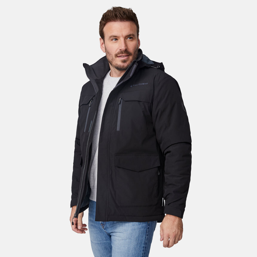 [Joe is 6'0" wearing size M.] Men’s Free Country black hooded utility jacket featuring dual zippered chest pockets, flap waist pockets, and rugged outdoor styling—paired with blue jeans for a functional, adventure-ready look.