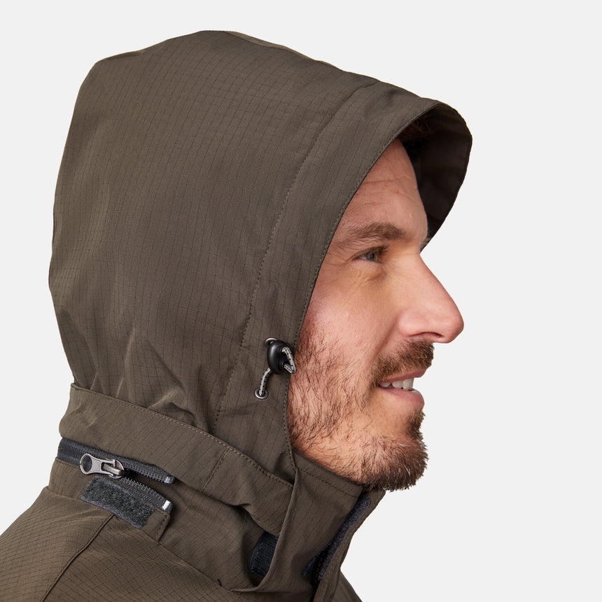 [Joe is 6'0" wearing size M.] Men’s Free Country brown hooded utility jacket featuring dual zippered chest pockets, flap waist pockets, and rugged outdoor styling—paired with blue jeans for a functional, adventure-ready look.