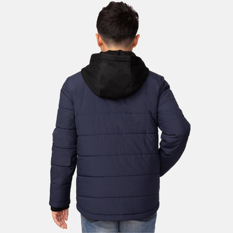 A person wearing a navy blue Free Country Boys' Trail Puffer Hoodie Shacket with a black hood, water resistant and shown from the back, is also dressed in blue jeans.