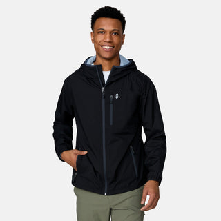[Josiah is 6'3" wearing a size Medium.] Man wearing the Free Country Men's Agile II Windshear Jacket in Black, size M, made from lightweight wind and water resistant recycled polyester fabric and featuring an attached hood, inner phone pocket and elastic cuffs, styled with a black t shirt and black pants #color_ black