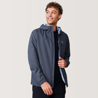 A man with curly hair smiles and looks to the side while wearing the Free Country Men's Agile II Windshear Jacket in dark gray over a black shirt, standing against a plain light background.
