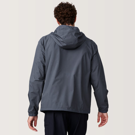 A man with curly hair is seen from behind wearing the Free Country Men's Agile II Windshear Jacket in gray with a hood, standing against a plain light background.