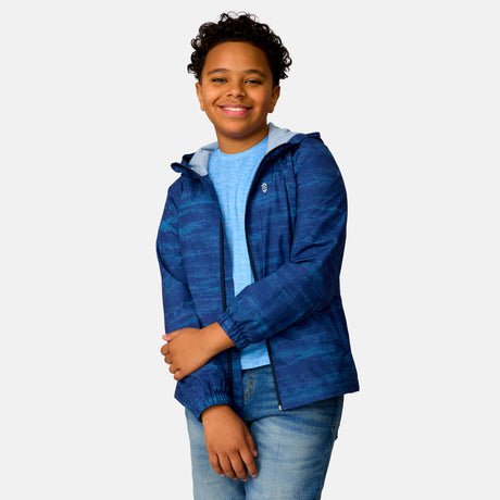 [Model is wearing a size Medium.] Boy wearing the Free Country Boys' Easy Hiking Windshear Jacket in Trail Patterns, size M, featuring lightweight wind and water resistant fabric and a full length zipper, paired with  blue jeans #color_ trail-patterns