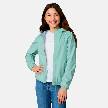A smiling girl wears the Clearance Girls' High Stretch Windshear Jacket in light blue over a white t-shirt and blue jeans, standing with one hand on her hip against a plain light gray background.
