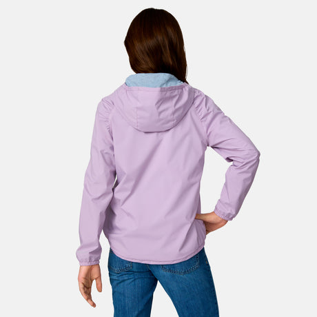 A girl with long brown hair is seen from behind in a Clearance Girls' High Stretch Windshear Jacket (light purple) and blue jeans, standing with one hand on her hip against a plain white background.