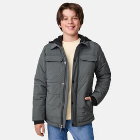 Smiling teenage boy wearing an evergreen Boys' Trail Puffer Hoodie Shacket by Clearance, featuring recycled synthetic fill, layered over a light yellow shirt and blue jeans, standing against a plain white background.