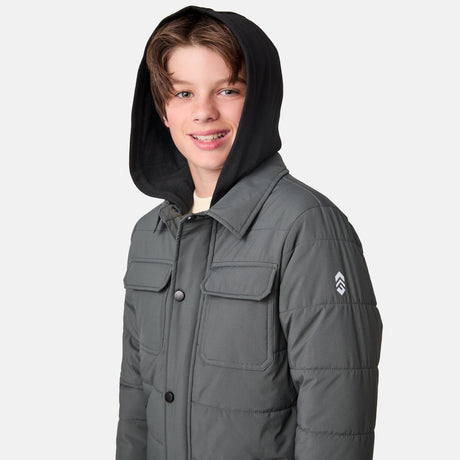 [River is wearing size M.] Model wearing a Free Country dark grey quilted hooded jacket featuring flap chest pockets, side hand pockets, and a partial front zip closure, paired with light innerwear and blue jeans—styled for casual outdoor comfort.