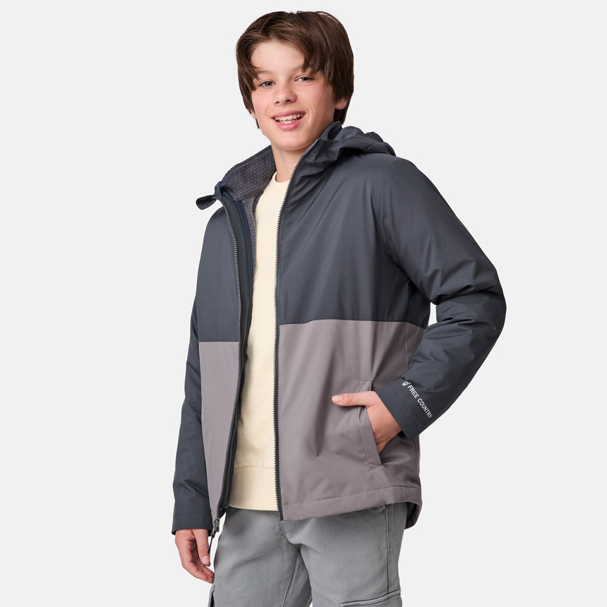 [River is wearing size M] Model in a two-tone Free Country system jacket featuring a dark gray upper shell and lighter gray lower body; complete with zip-out fleece liner, side-entry pockets, and an adjustable hood—styled with tonal gray pants for streamlined, cold-weather versatility.