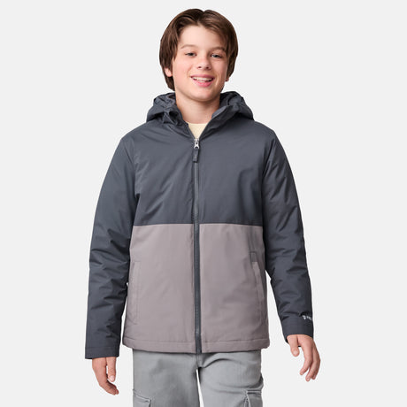 [River is wearing size M] Model in a two-tone Free Country system jacket featuring a dark gray upper shell and lighter gray lower body; complete with zip-out fleece liner, side-entry pockets, and an adjustable hood—styled with tonal gray pants for streamlined, cold-weather versatility.