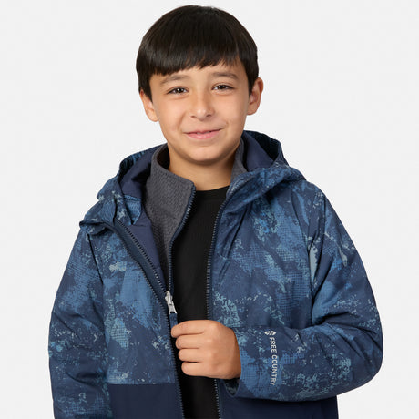 A boy wears a blue patterned Boys’ High Stretch 3-in-1 Systems Jacket over a grey zip-up layer and a black shirt.