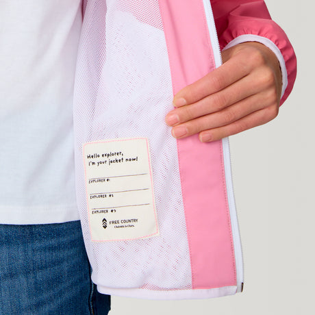 [Model is wearing a size Medium.] Girl wearing the Free Country Girls' Easy Hiking Windshear Jacket in Rose Petal, size M, featuring two tones color made from recycled polyester fabric that provides four way stretch and water and wind resistance, layered over a white t shirt with blue jeans #color_ Rose-Petal