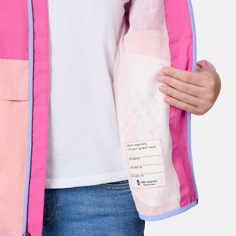 A person in blue jeans and a white shirt displays the mesh lining and label of the Free Country Girls' Easy Hiking Windshear Jacket, highlighting details of this lightweight pink and purple outdoor windbreaker.