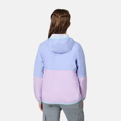 A person with long, braided hair is seen from behind wearing the Free Country Girls' Easy Hiking Windshear Jacket in pastel purple and pink, paired with light gray cargo pants, standing against a plain white background.