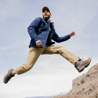Man in outdoor attire jumping in a mountainous area
