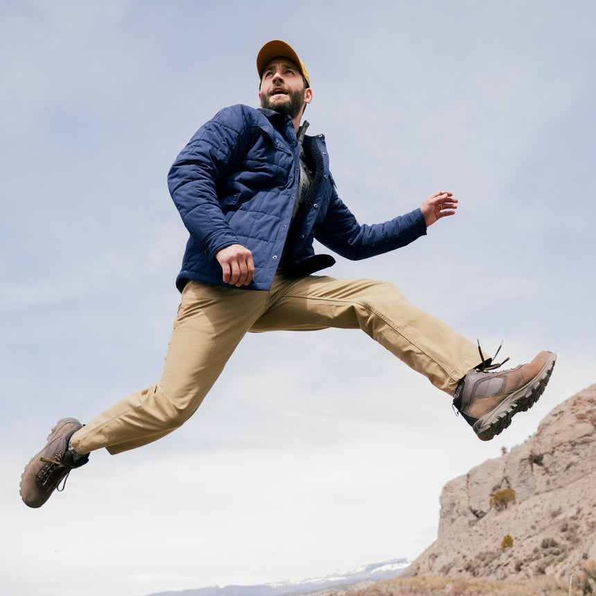 Man in outdoor attire jumping in a mountainous area