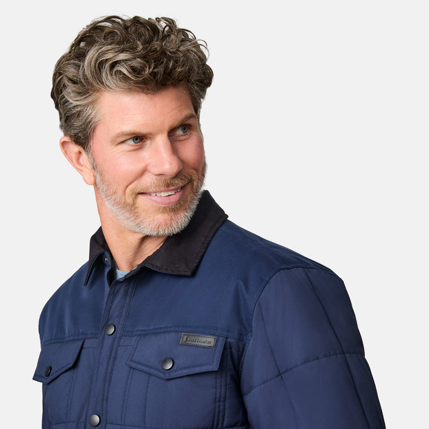 [Kolby is 6'2" wearing size M.] Men’s Free Country dark blue quilted jacket with button-up front, flap chest pockets, and contrasting corduroy-style collar—styled with light-colored pants for a rugged, heritage-inspired outdoor look.