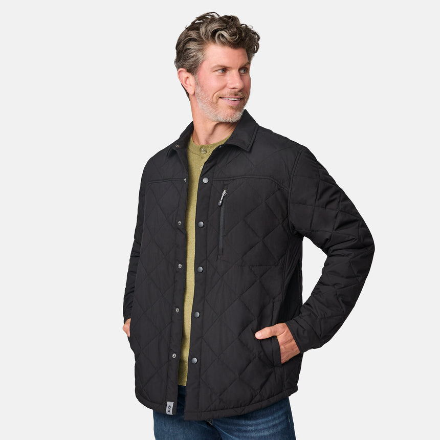 [Kolby is 6'2" wearing size M.] Men’s Free Country black quilted jacket with diamond pattern stitching—featuring button front closure, zippered left chest pocket, and side hand pockets. Layered over a green crewneck tee and blue jeans for a laid-back, outdoors-ready aesthetic.