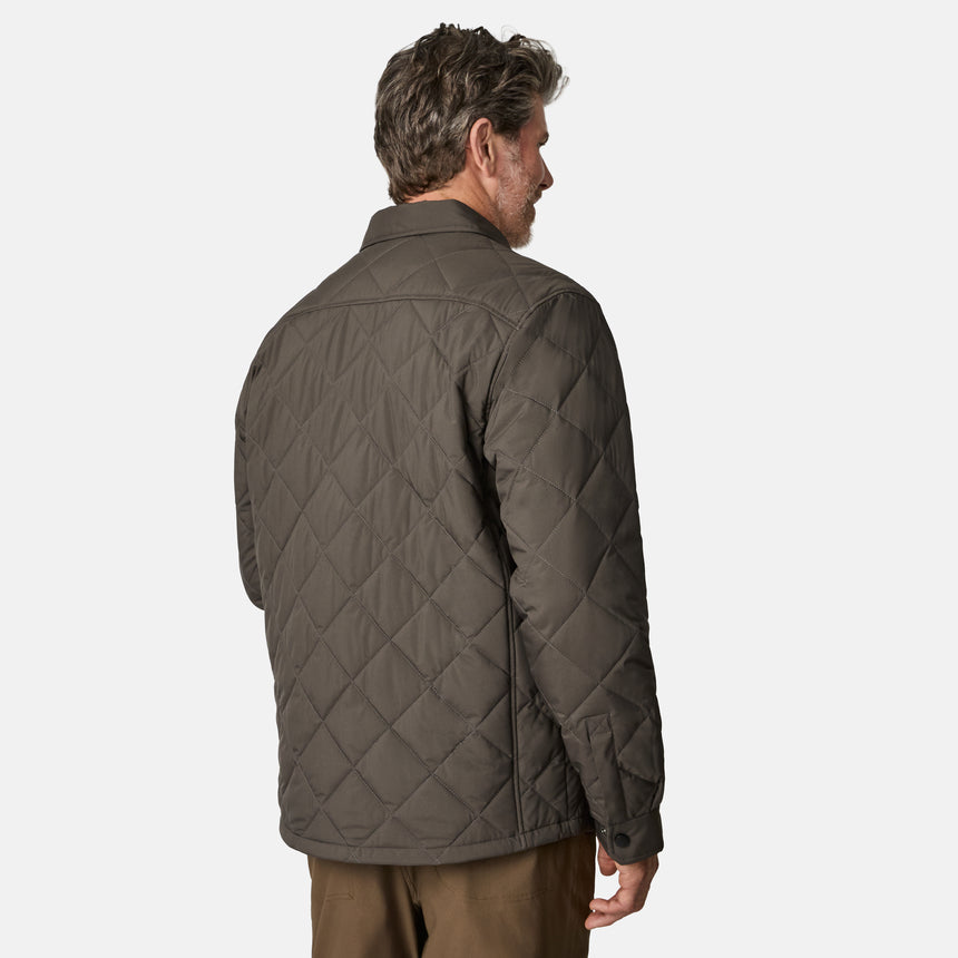 [Kolby is 6'2" wearing size M.] Men’s Free Country quilted jacket in brown with diamond pattern stitching—features a zippered left chest pocket, button front closure, and side hand pockets. Styled over a light gray shirt and paired with brown pants for a rugged, polished outdoor look.