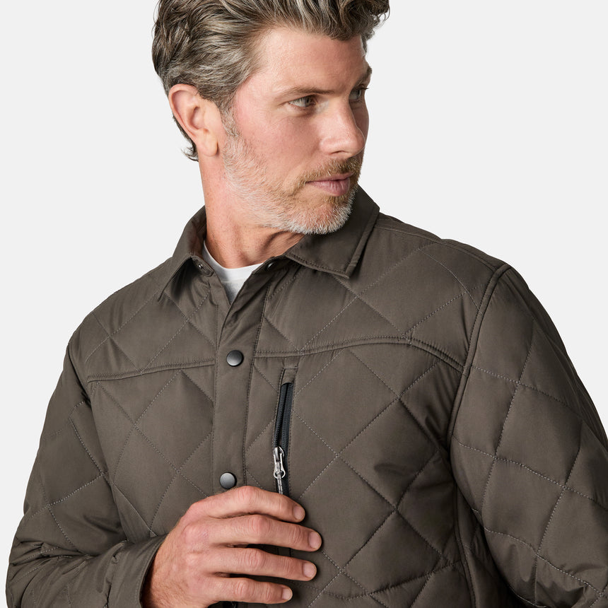 [Kolby is 6'2" wearing size M.] Men’s Free Country quilted jacket in brown with diamond pattern stitching—features a zippered left chest pocket, button front closure, and side hand pockets. Styled over a light gray shirt and paired with brown pants for a rugged, polished outdoor look.